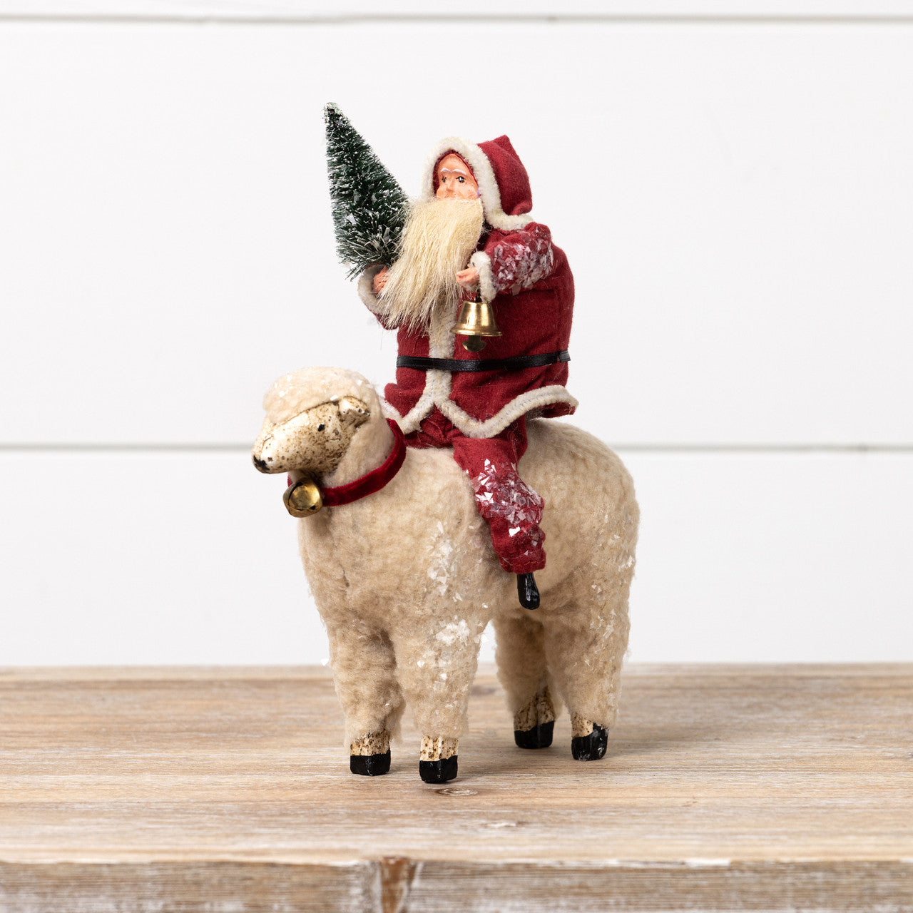 Decorative figure of Santa Claus riding a sheep with a Christmas tree on its back, on a wooden surface.