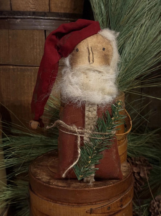 A rustic Christmas decorative figure resembling Santa Claus, made from a wooden face with white faux fur for a beard, wearing a red hat and brown body, displayed on a wooden barrel with pine branches in the background.