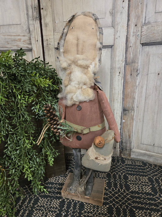 Decorative Santa with a beard and hat, standing on a wooden floor with greenery.