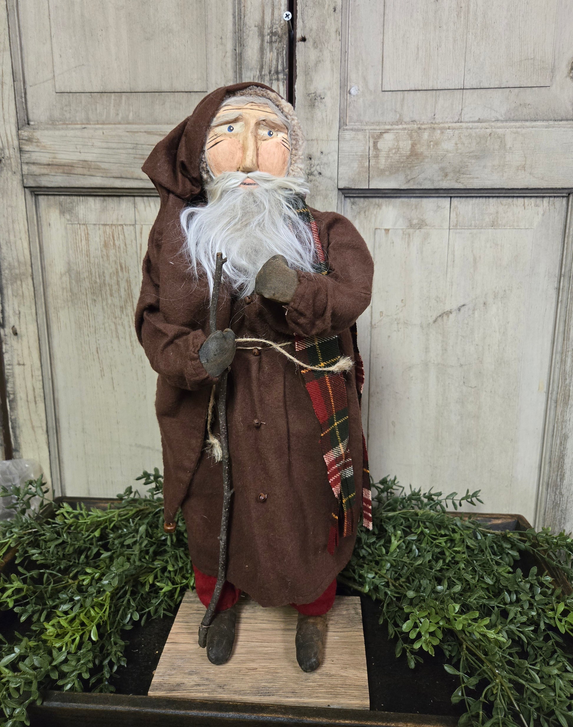 Clay face Santa with a white beard in brown coat holding a walking stick