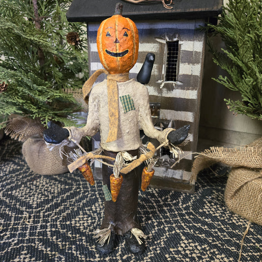 A handcrafted scarecrow with a pumpkin face and a bird perched on its glove, set against a rustic background.