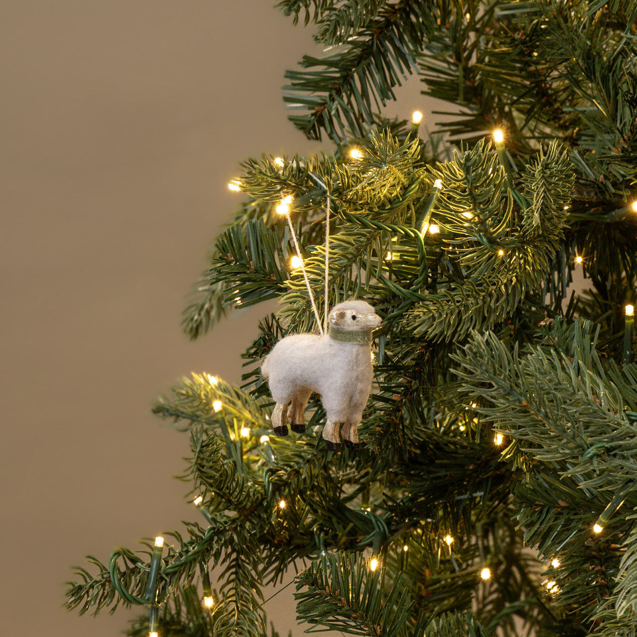 White sheep ornament on a decorated Christmas tree with lights.