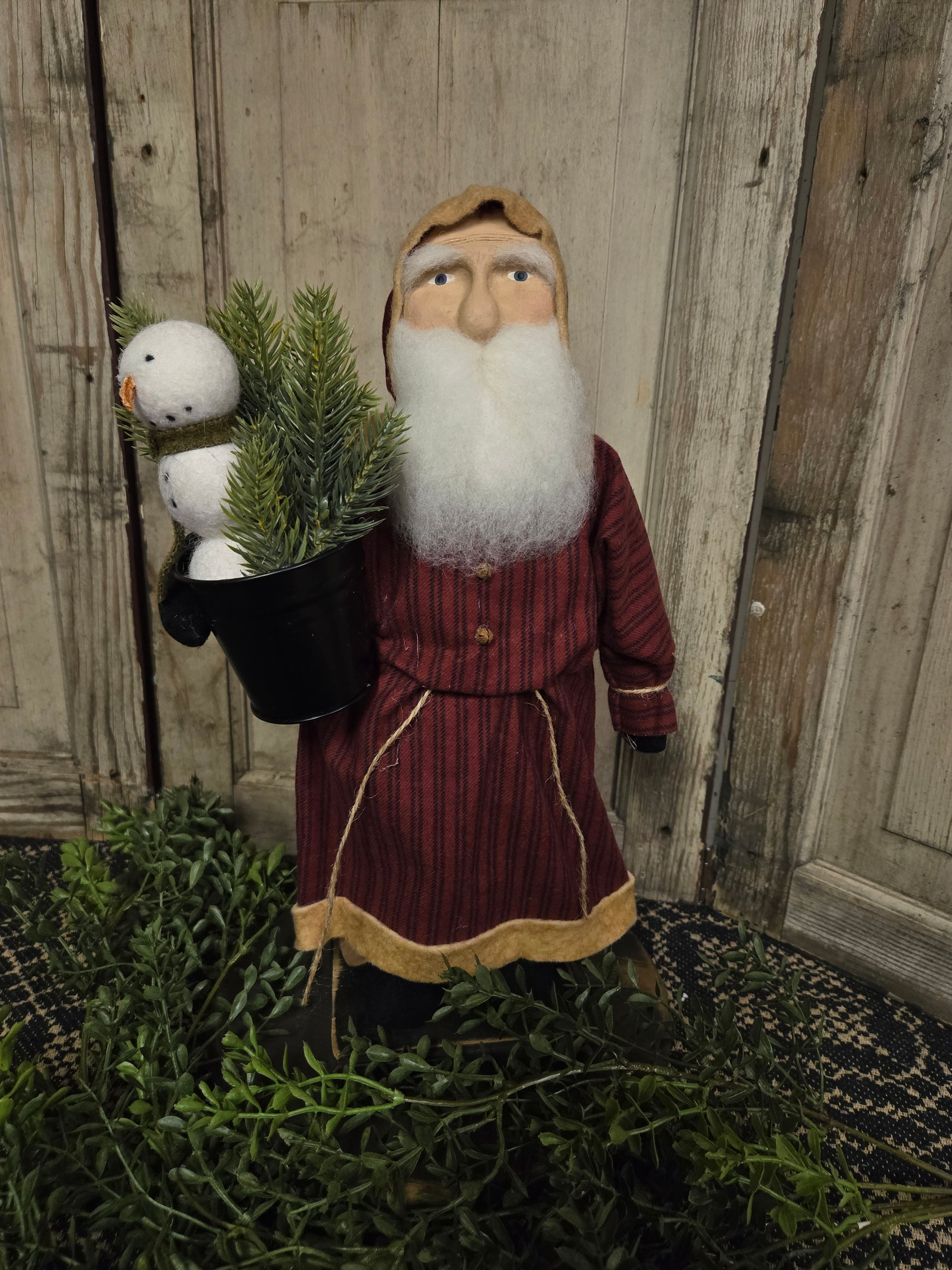 Clay faced santa in a red, striped coat holding a flower pot with greenery and a snowman