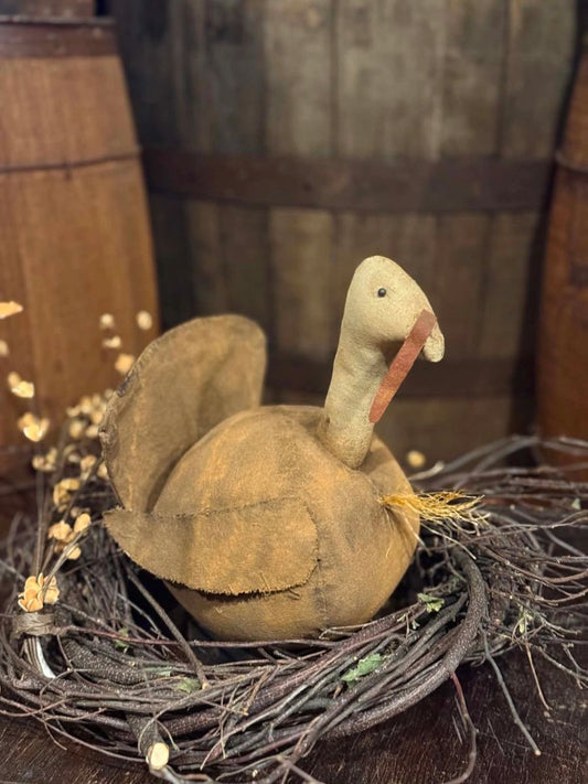 A rustic handmade duck figurine made from natural wood and fabric, perched on a twig wreath with dried flowers, set against a background of wooden barrels.