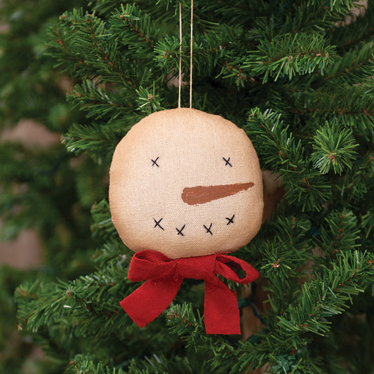 Primitive snowman head ornament with red scarf hanging from a Christmas tree