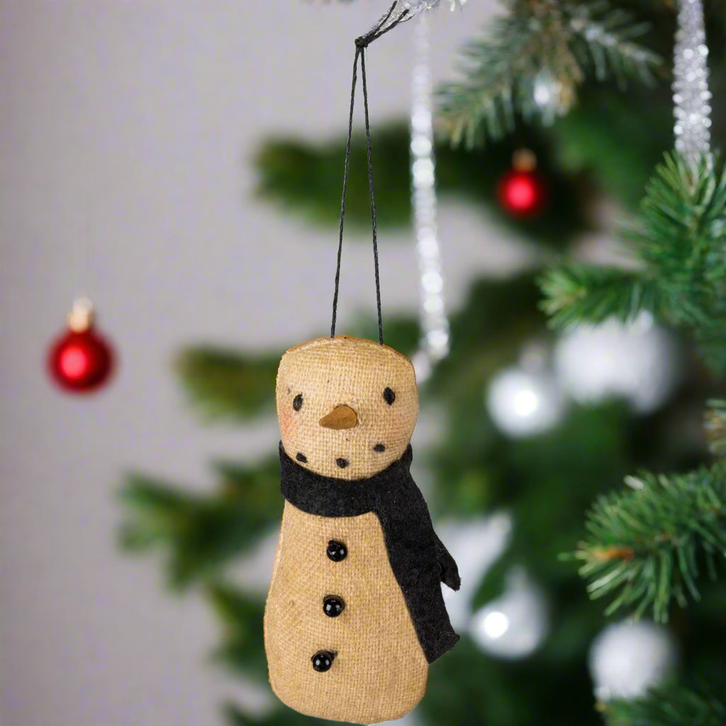 A beige fabric snowman ornament with a black scarf, designed for hanging as a holiday decoration.