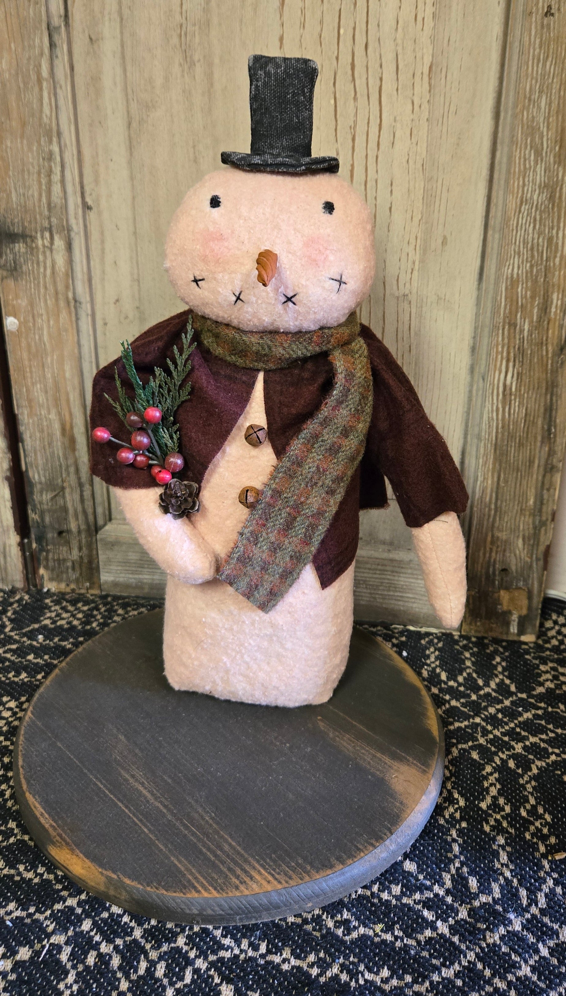 A handcrafted 12 inch snowman decoration with a top hat, made with cotton batting and flannel attire, displayed against a rustic backdrop.