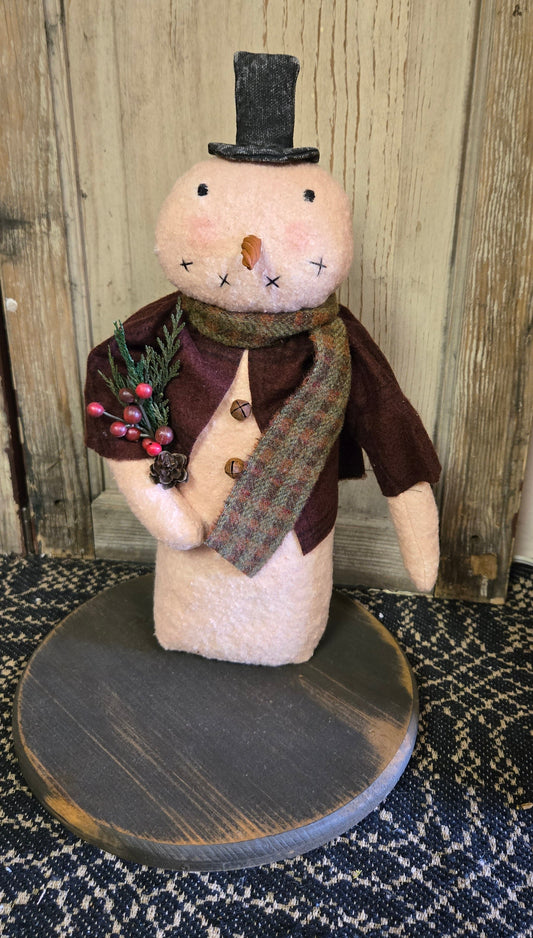 A handcrafted 12 inch snowman decoration with a top hat, made with cotton batting and flannel attire, displayed against a rustic backdrop.