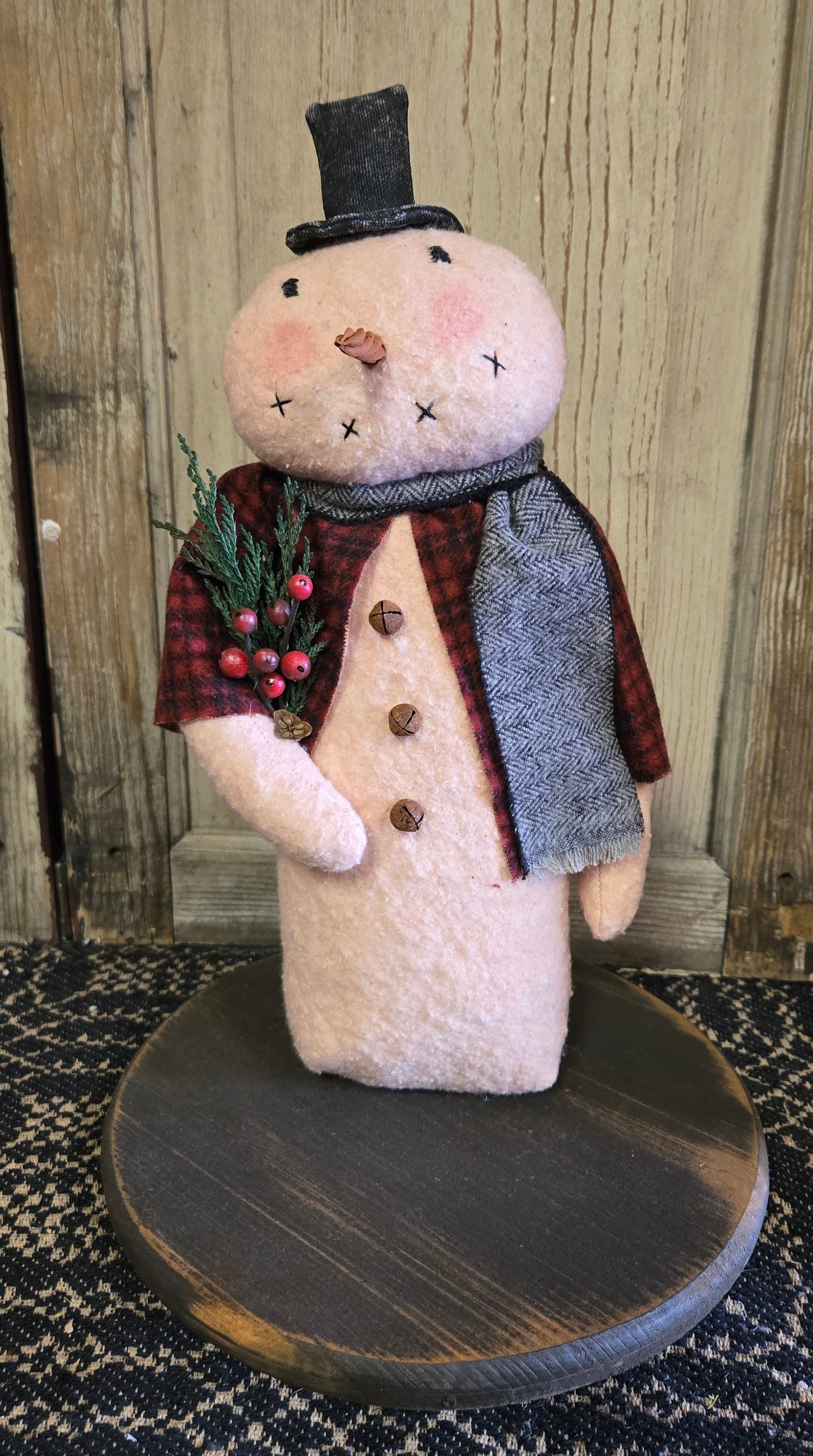 A 12-inch snowman decoration with a top hat, made of cotton batting and adorned with flannel attire, cedar, pinecone, and berries.