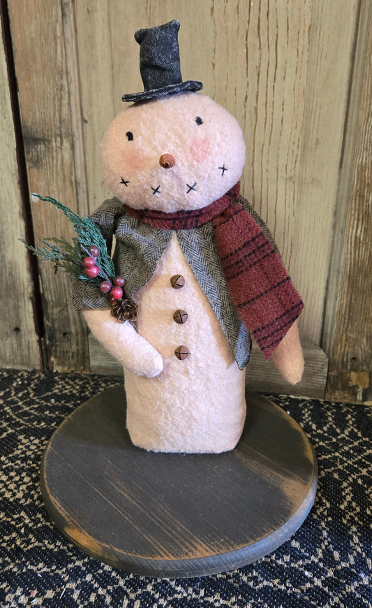 A 12 inch snowman decoration with a top hat, made of cotton batting, with a rustic coffee stain, flannel attire, and adorned with pinecones and berries.