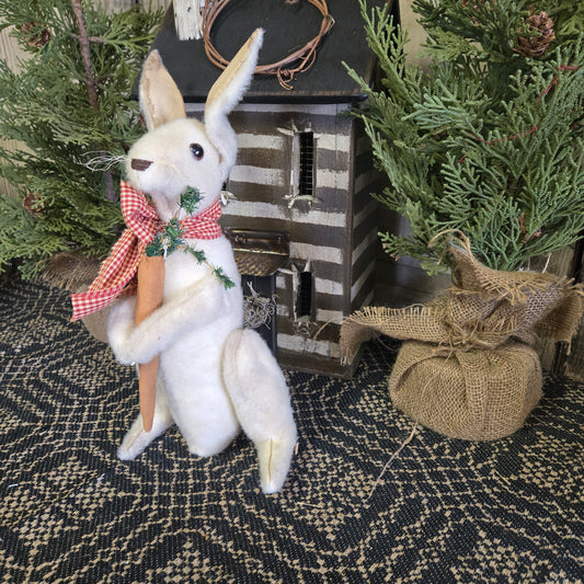A handcrafted standing bunny with a carrot, wearing a red and green scarf, placed among decorative greenery.