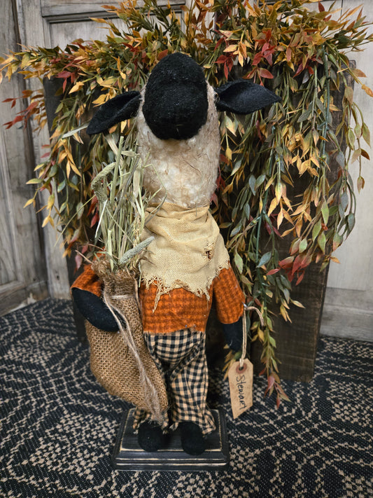 Decorative sheep figure with plaid outfit and black boots on a textured surface with foliage.