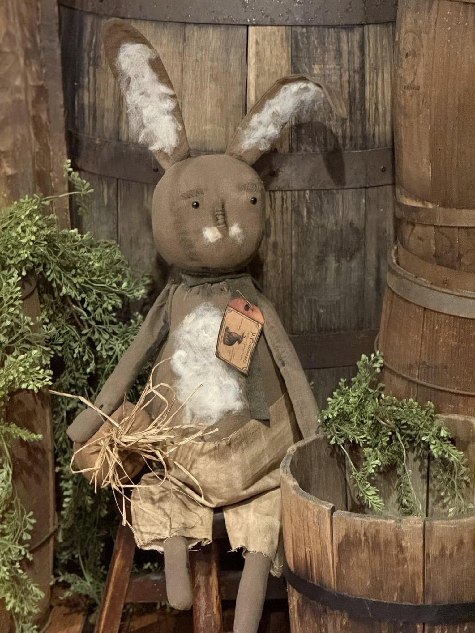 A plush toy depicting a brown bunny with a white belly, holding a carrot and sitting upright against a wooden backdrop.