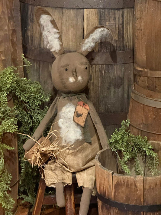 A plush toy depicting a brown bunny with a white belly, holding a carrot and sitting upright against a wooden backdrop.
