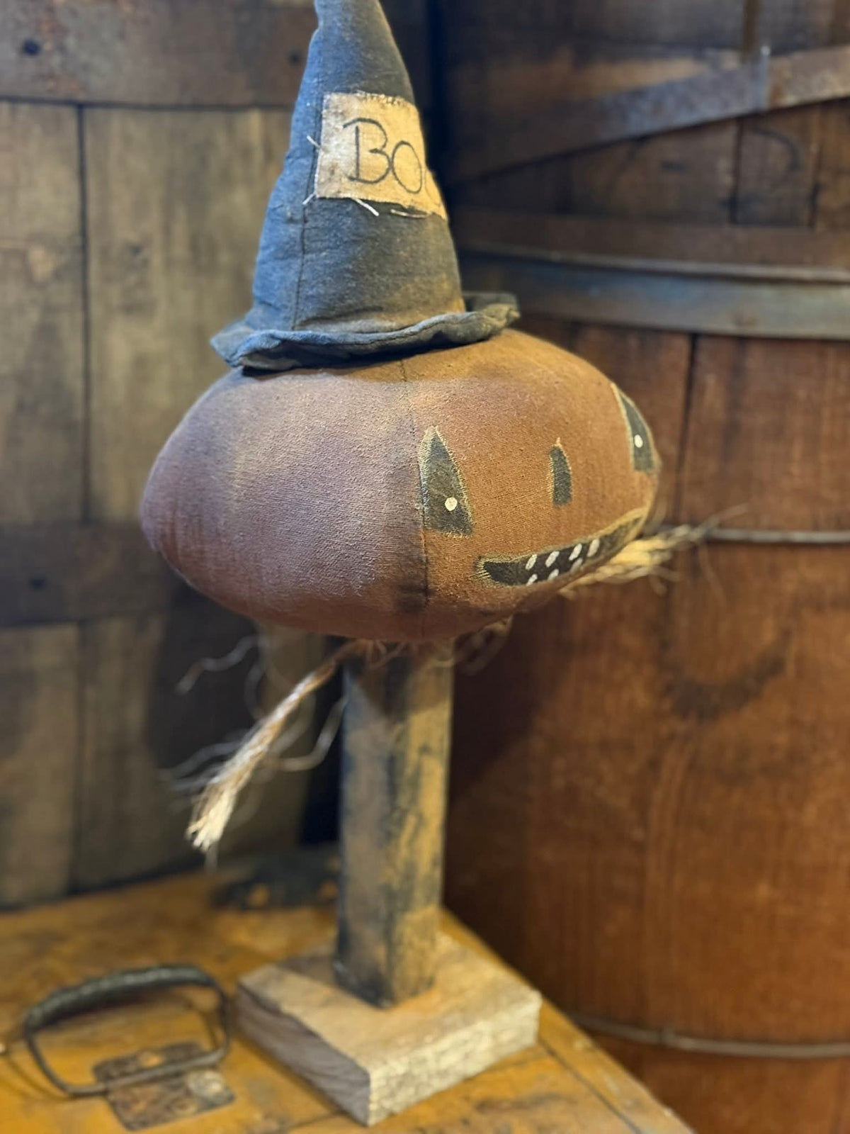 Decorative pumpkin with a witch hat and carved face on a wooden base against a rustic wooden background.