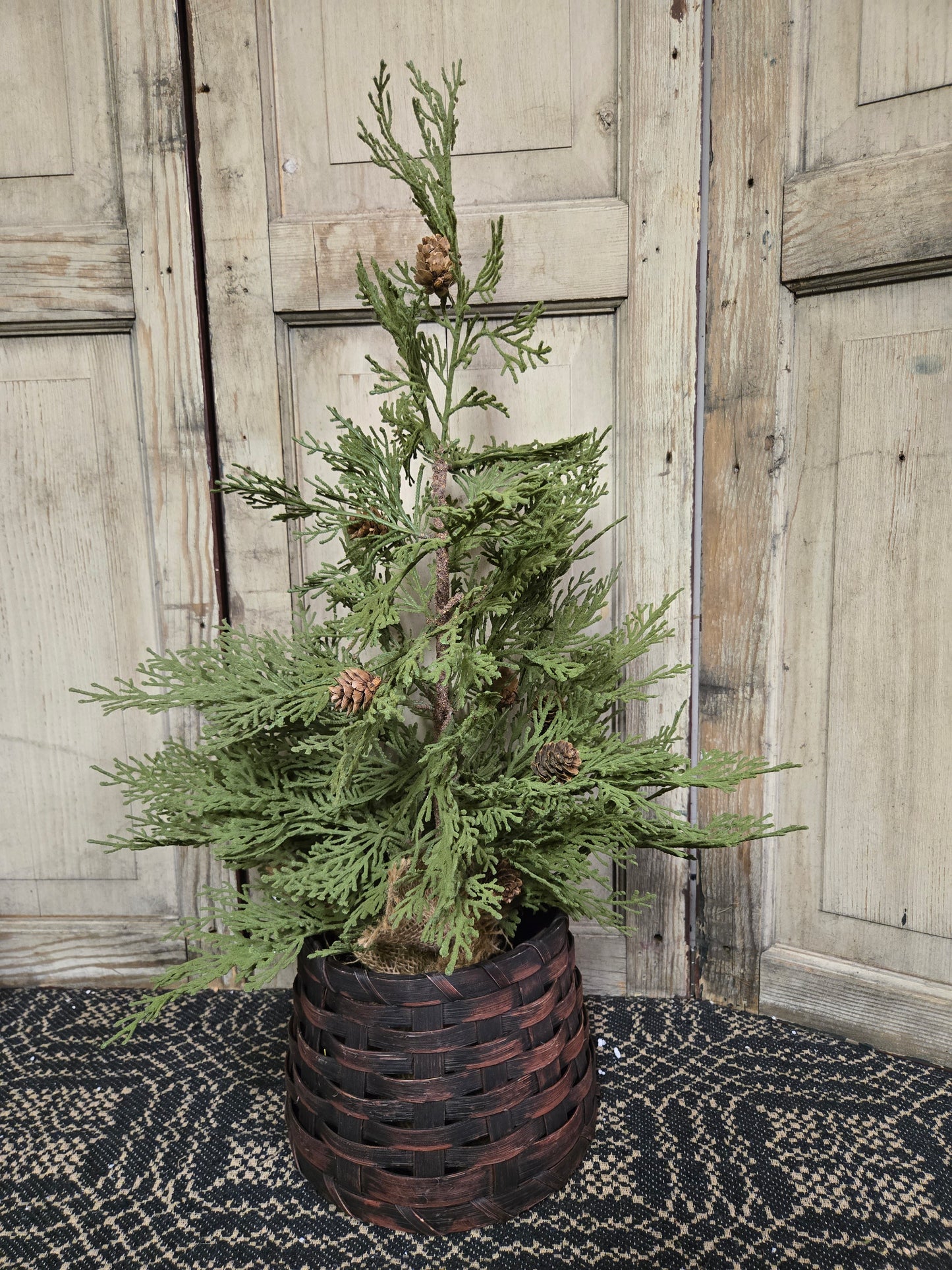 A small burgundy primitive basket designed to hold a twig tree, displayed against an old wooden door background.
