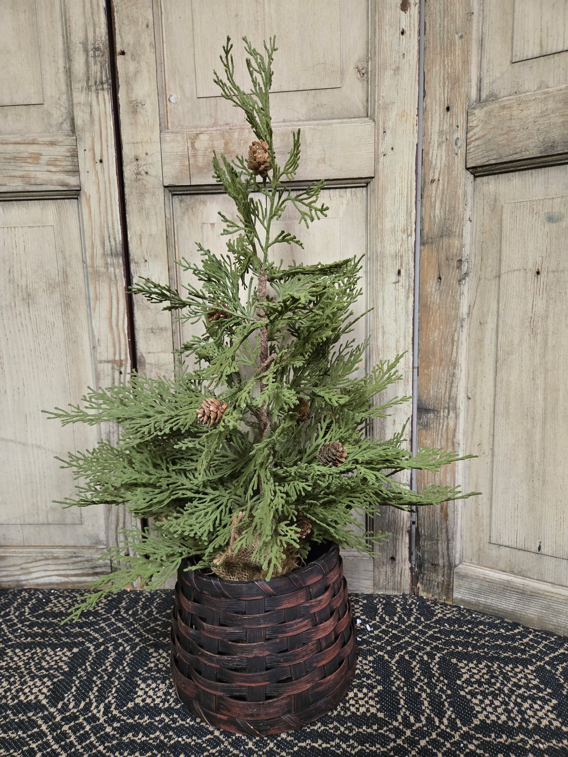 A small burgundy primitive basket designed to hold a twig tree, displayed against an old wooden door background.