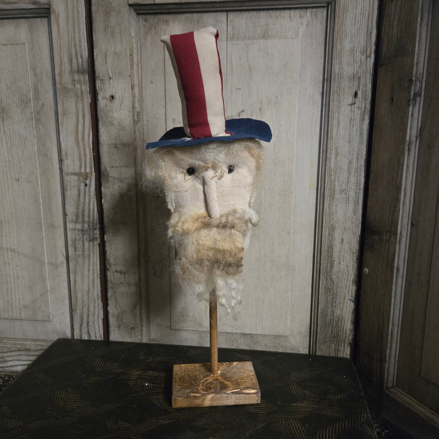 Vintage-style uncle sam head with a patriotic hat on a stand against a wooden paneled wall.