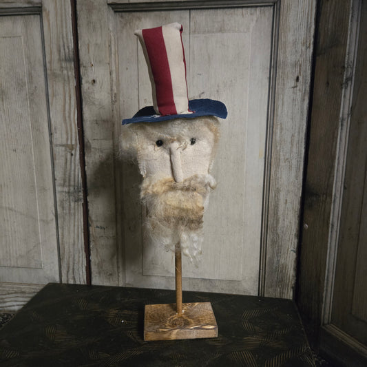 Vintage-style uncle sam head with a patriotic hat on a stand against a wooden paneled wall.