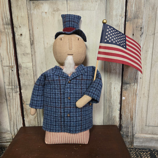 Small figurine wearing a blue coat and holding an American flag on a wooden surface