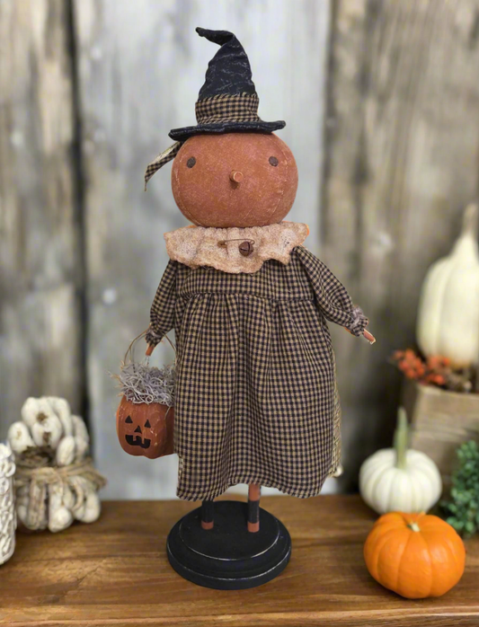 Decorative figure of a person in a checkered dress and witch hat with a pumpkin, on a wooden surface.