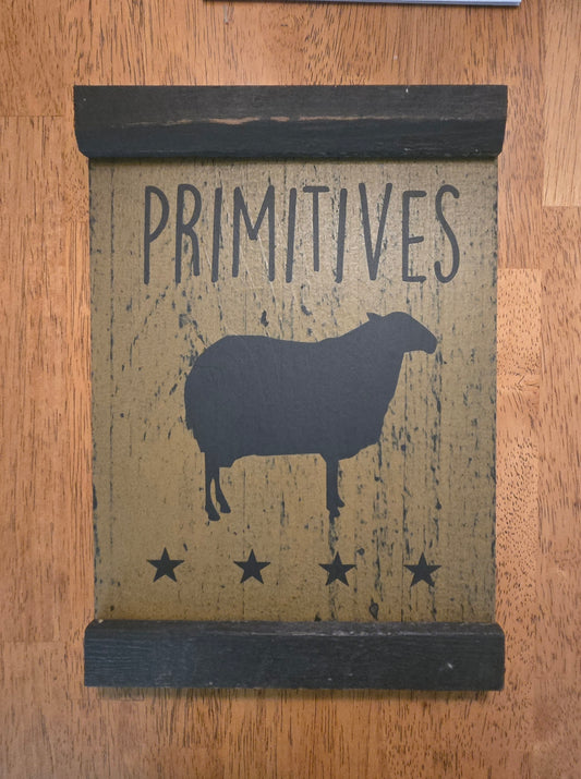 Decorative sign with 'PRIMITIVES' and a sheep silhouette on a wooden background
