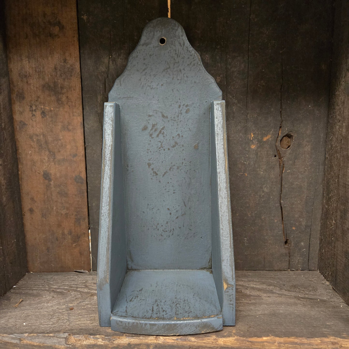 A vintage style wood sconce with a distressed blue-gray finish, set against a rustic dark wood background.