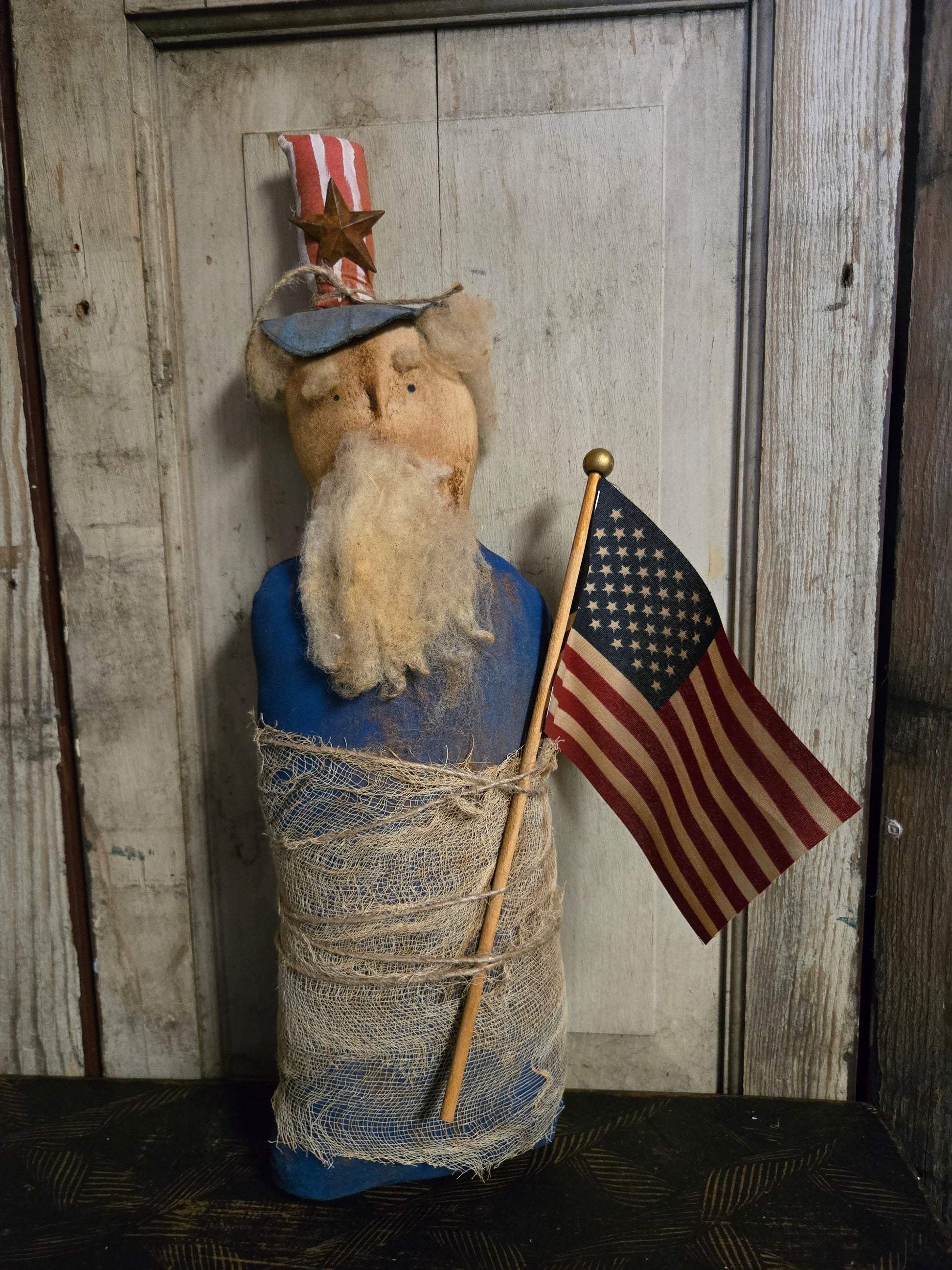 Vintage-style figure wrapped in blue fabric with an American flag against a wooden background