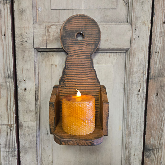A rustic wooden wall sconce mounted on a door, holding a lit candle, with visible wood grain and craftsmanship.