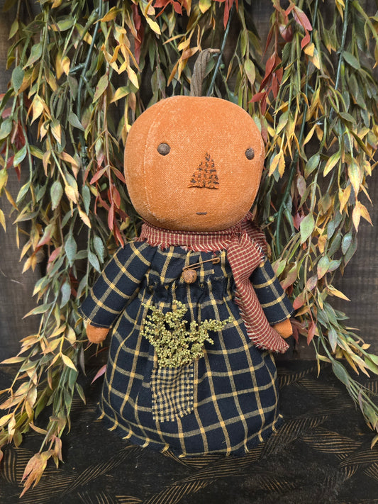 Textile doll with plaid dress and brown head against a leafy background