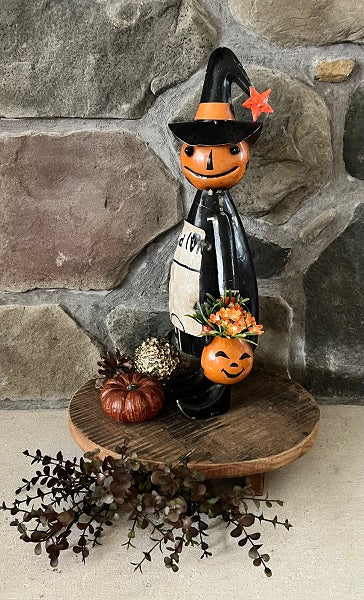 Metal pumpkin girl holding pumpkin pail standing on wood riser