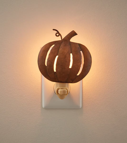 Pumpkin night light plugged into outlet on beige background