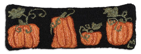 A rectangular hooked wool pillow with an orange pumpkin design and green vines on a black background, with a velveteen backing.