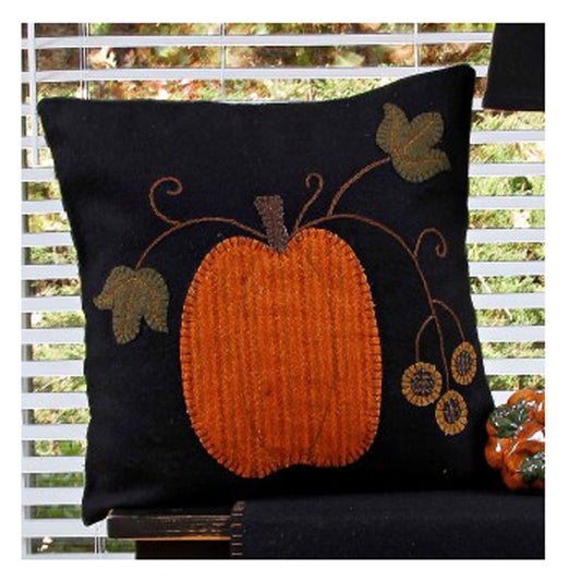 A pumpkin-shaped throw pillow with an embroidered design, placed on a chair with a window in the background.