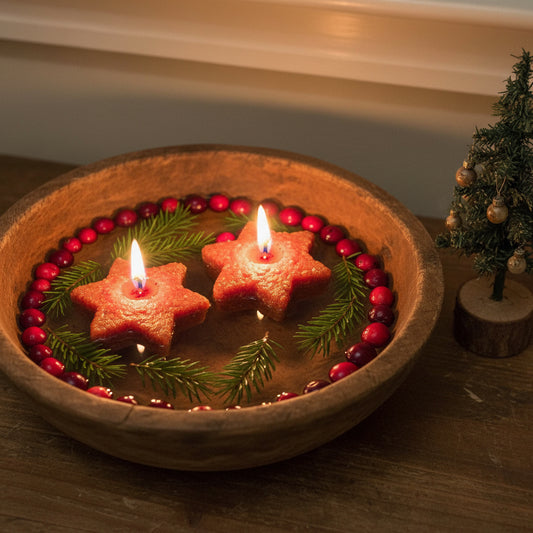 Star-shaped cookies with candles in a wooden bowl with berries and greenery, next to a small Christmas tree.
