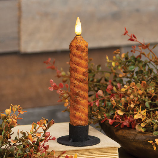 A pumpkin-colored flameless candle with a vintage twist flicker flame, placed on a book, with autumn leaves and a wooden background.