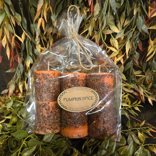 Six pumpkin spice candles in packaging on a green leafy background