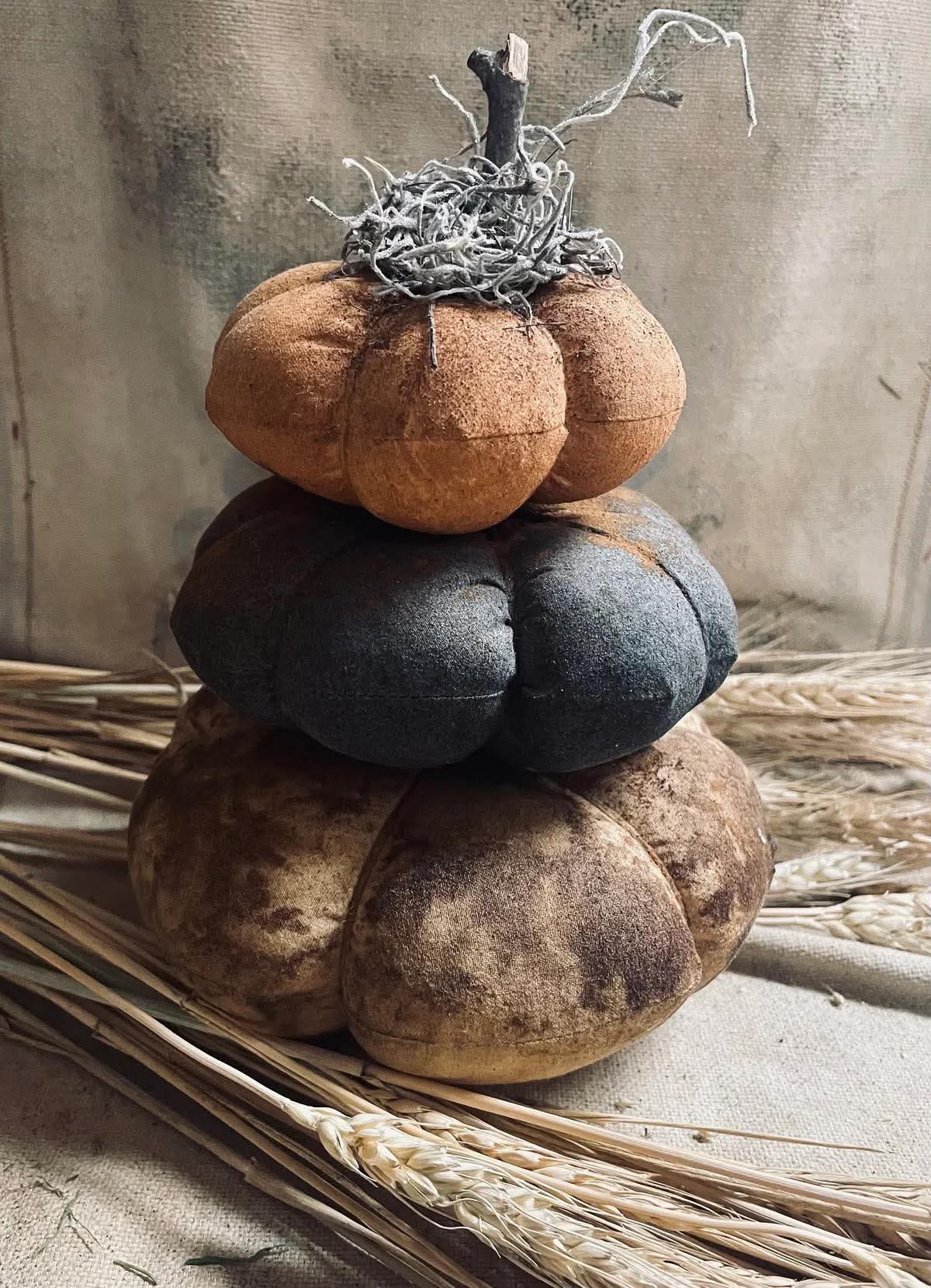 Stack of fabric pumpkins in brown, blue, and beige with a rustic background.
