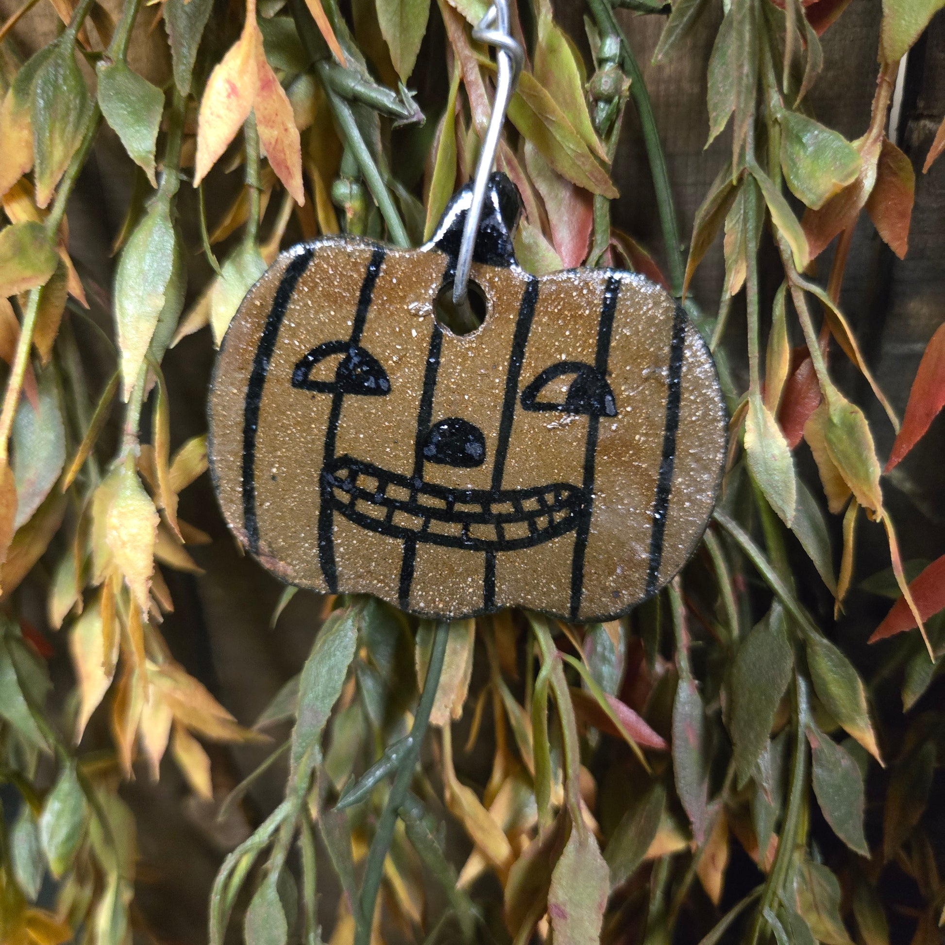 Striped pumpkin stoneware ornament with Jack O'Lantern face on greenery