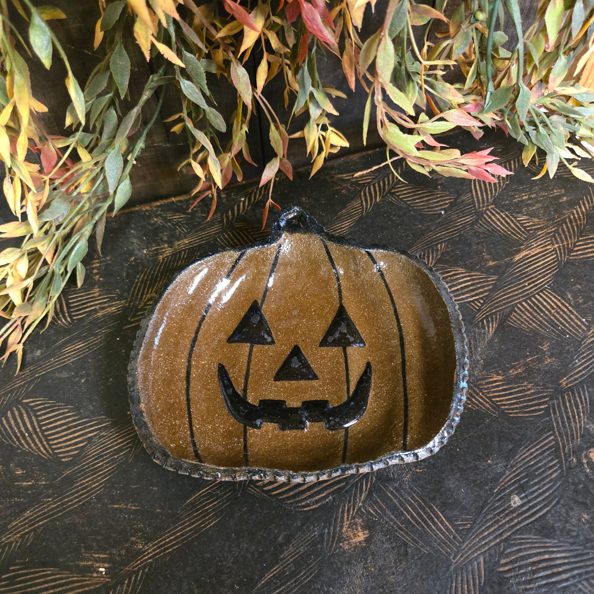 Decorative pumpkin shape plate with face design on a textured surface with leaves.