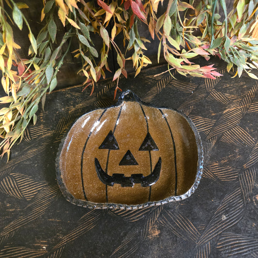 Decorative pumpkin shape plate with face design on a textured surface with leaves.