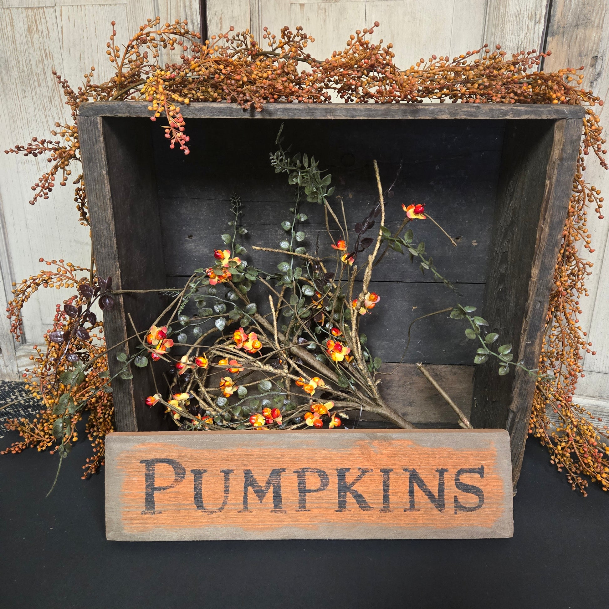 Decorative wooden box with dried flowers and a 'Pumpkins' sign on a dark background.