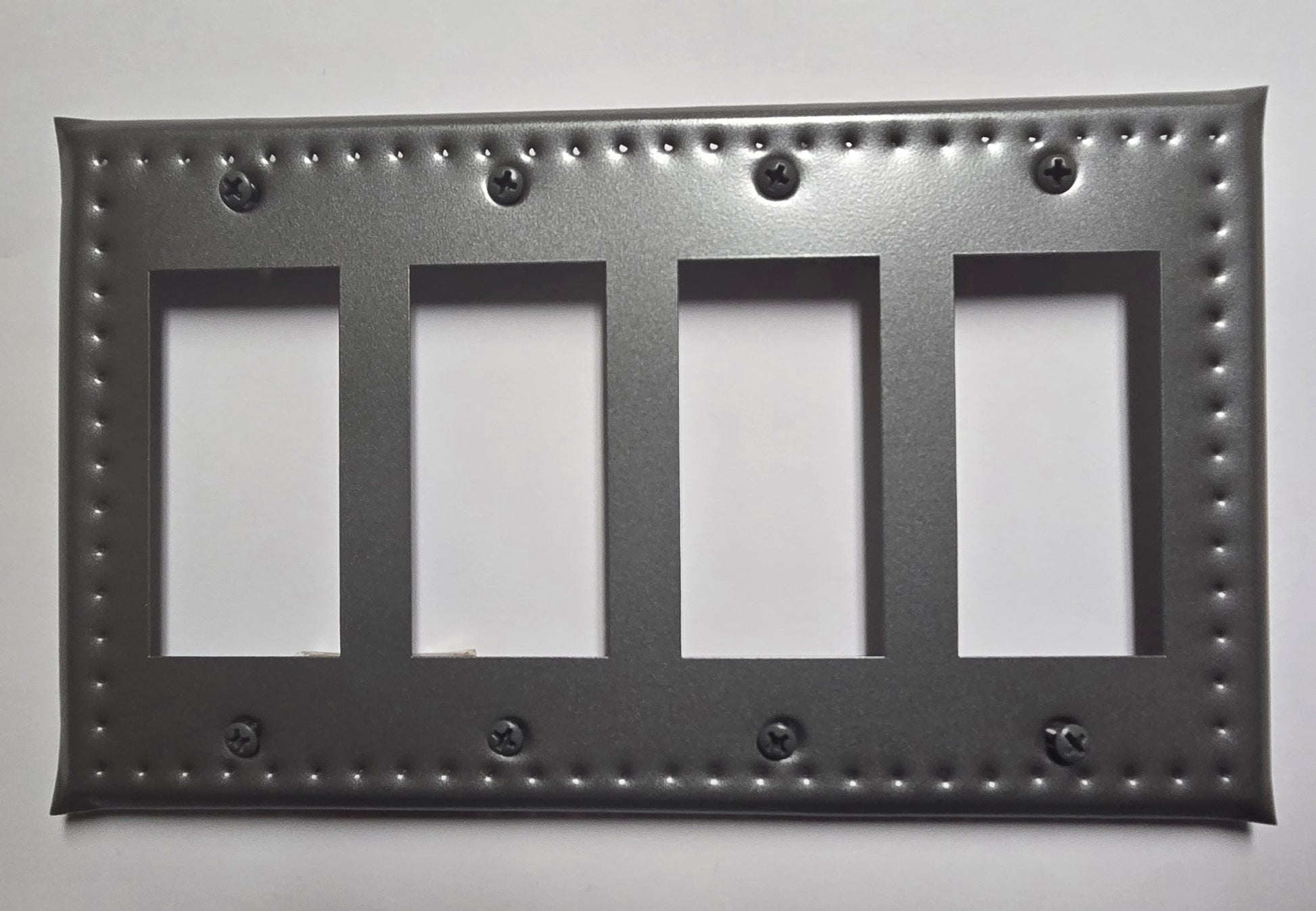 Decorative black metal switch plate with four blank panels on a white background