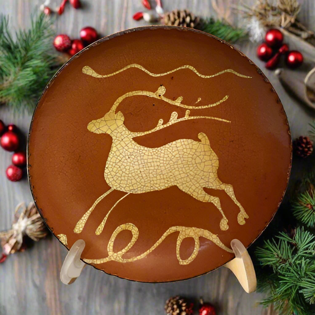 A brown ceramic plate with a hand-quilled leaping stag design displayed on a stand.