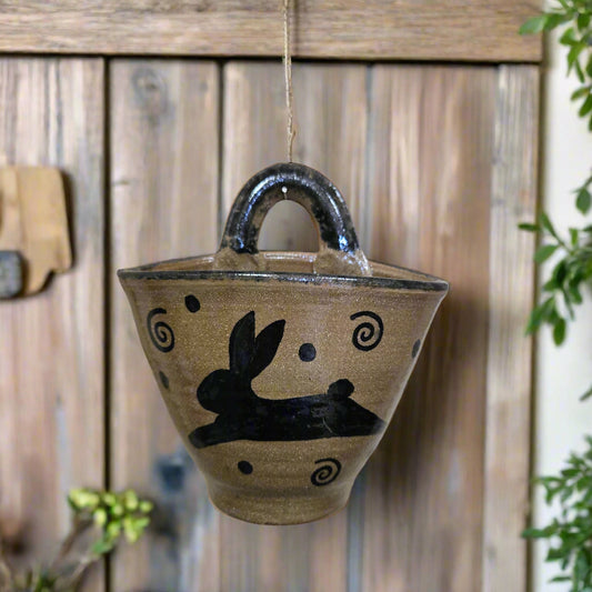 A handcrafted stoneware wall pocket with a brown base color and black rabbit pattern, mounted on a wooden surface.