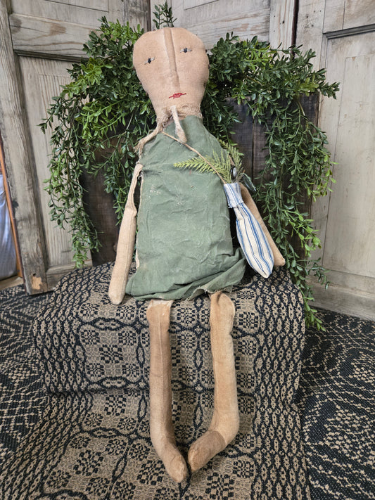 Vintage-style doll with green dress and striped headband leaning against a textured wall.