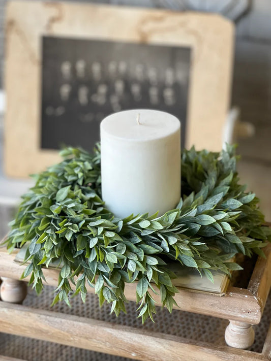 White candle in a green wreath on a wooden surface with a blurred background