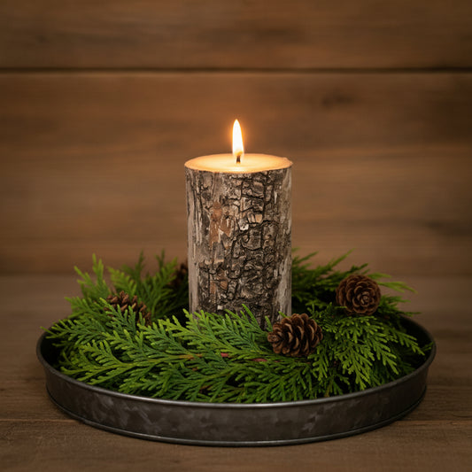 Candle in a tree bark holder on a bed of greenery with a wooden background