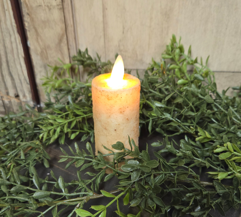 Flickering candle on a bed of greenery with a wooden background