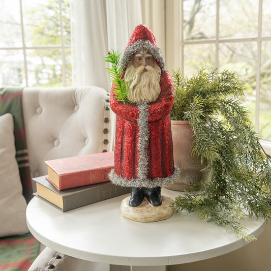 Decorative figure of a bearded man in a red outfit on a table with books and greenery.